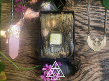 time crystal quartz crystal amulet necklace front view photographed laying between the samadhi rose quartz crystal amulet necklace and the egyptian goddess isis pendant necklace made by chateau de lion cdl-neck-tm-001